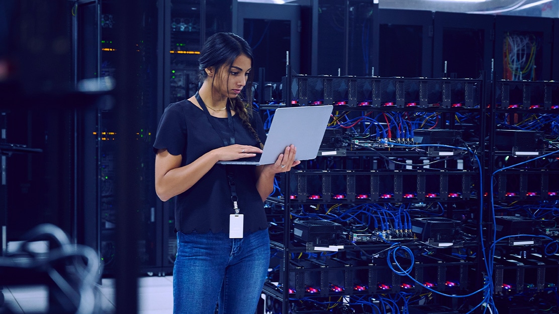 Employee in a server room reviewing content on a laptop. 