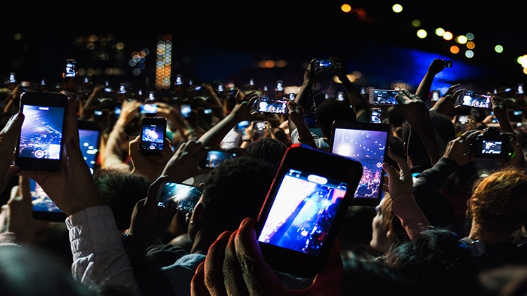 Crowd at a concert holding up smartphones to record the performance